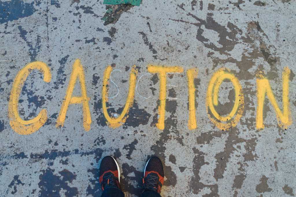 Caution written in chalk on a pavement with a person in running shoes standing in front
