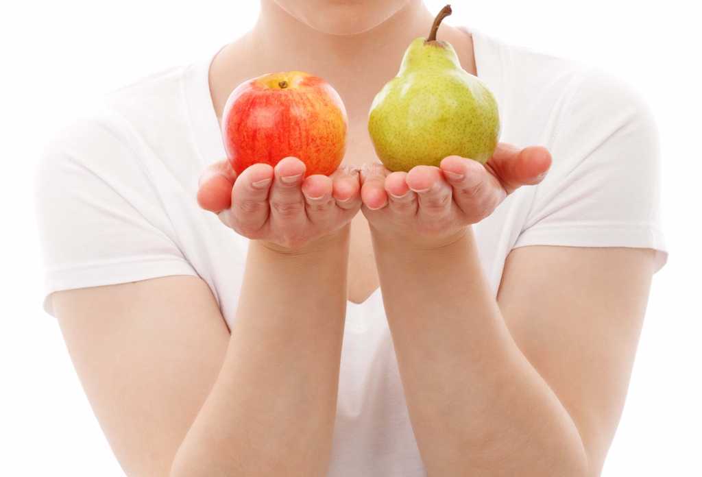 woman holds an apple in one hand and pear in the other in front of her body with white background