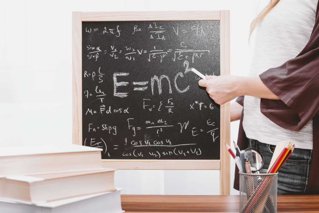 Student uses stick of chalk to point towards a blackboard reading E=MC^2