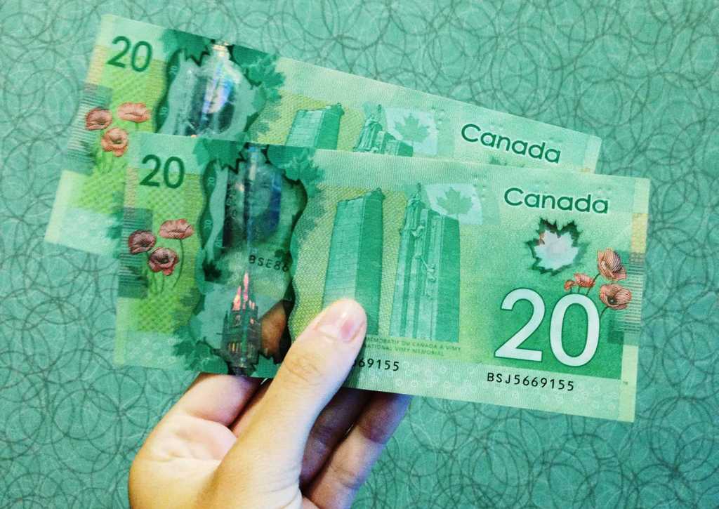 hand holding two Canadian twenty dollar bills over green patterned floor