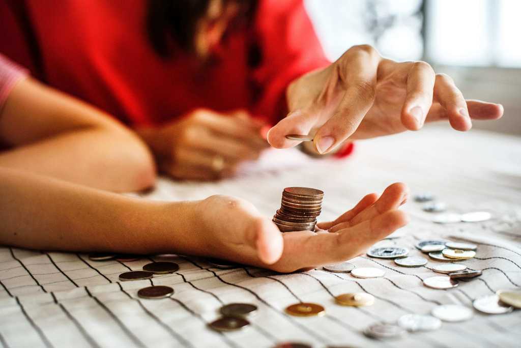 Woman places penny on a stack of pennies in a child's hand above a table with various coins placed on top