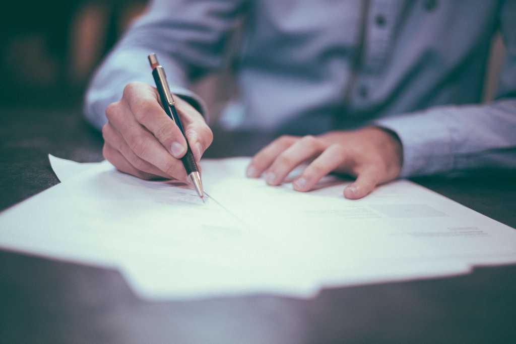 Male professional signs mortgage refinancing contracts with a nice pen above a dark wooden table 