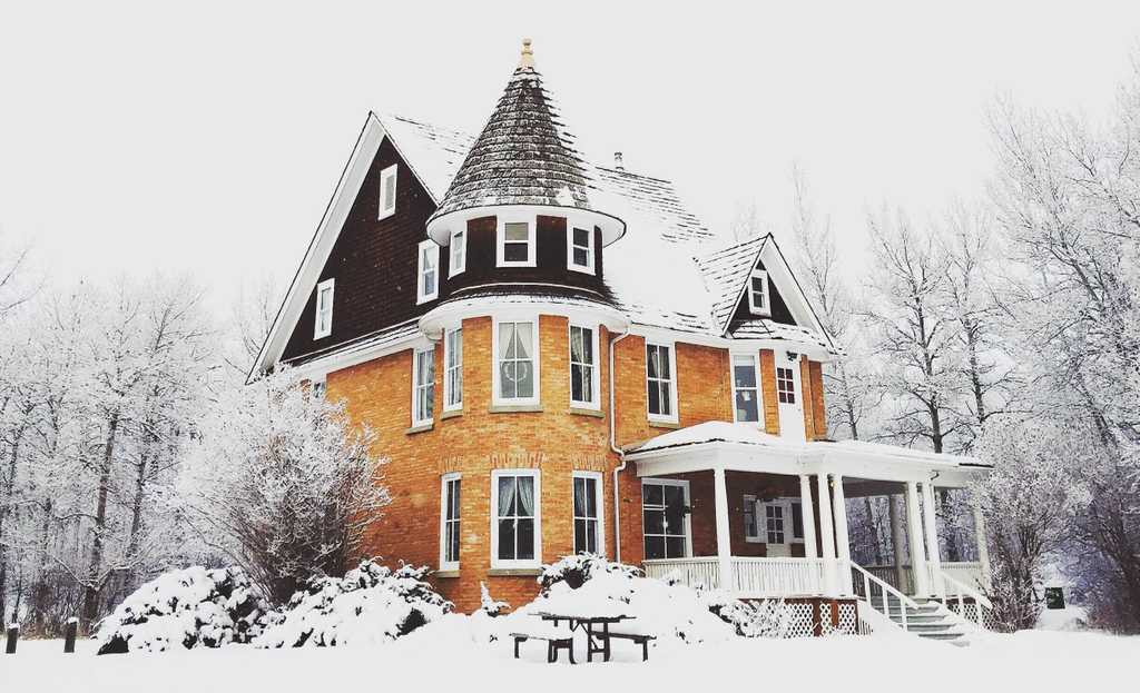 yellow house sits in a beautiful forest covered in snow on a cloudy day