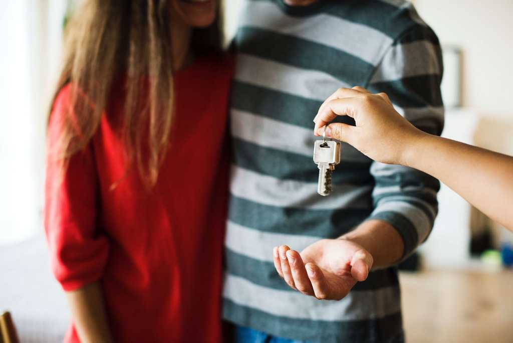 hand extends to pass keys to the blue and white striped shirted male beside a red shirted female